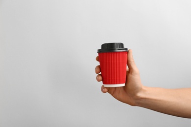 Man holding takeaway paper coffee cup on light background. Space for design