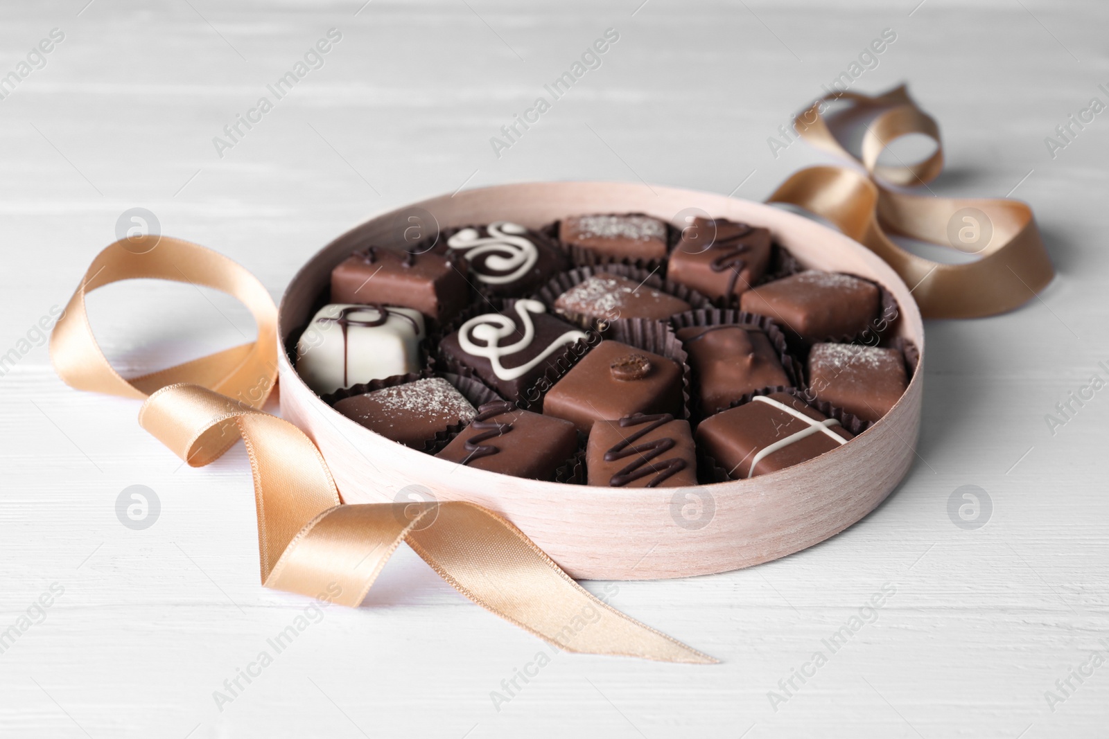 Photo of Delicious chocolate candies in box on white wooden table