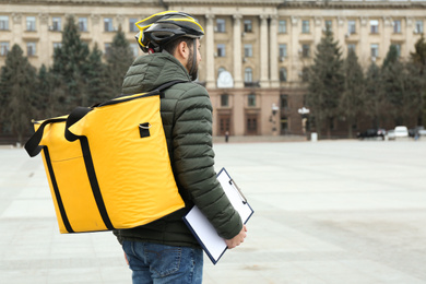 Courier with thermo bag and clipboard on city street. Food delivery service