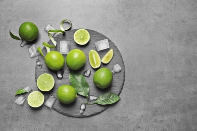 Photo of Slate plate with fresh ripe limes and ice cubes on gray background, top view