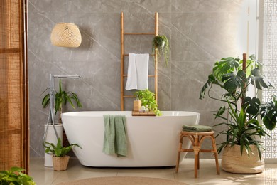 Modern white tub and beautiful green houseplants in bathroom. Interior design