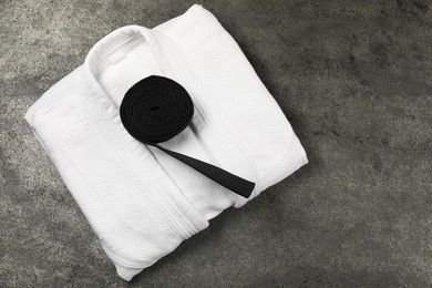 Photo of Black karate belt and white kimono on gray textured background, top view. Space for text