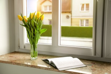 Photo of Bouquet of beautiful yellow tulip flowers in glass vase and open book on windowsill. Space for text