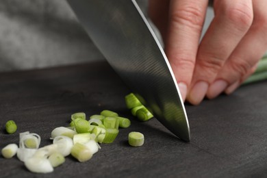 Photo of Woman cutting green spring onion on black wooden board, closeup