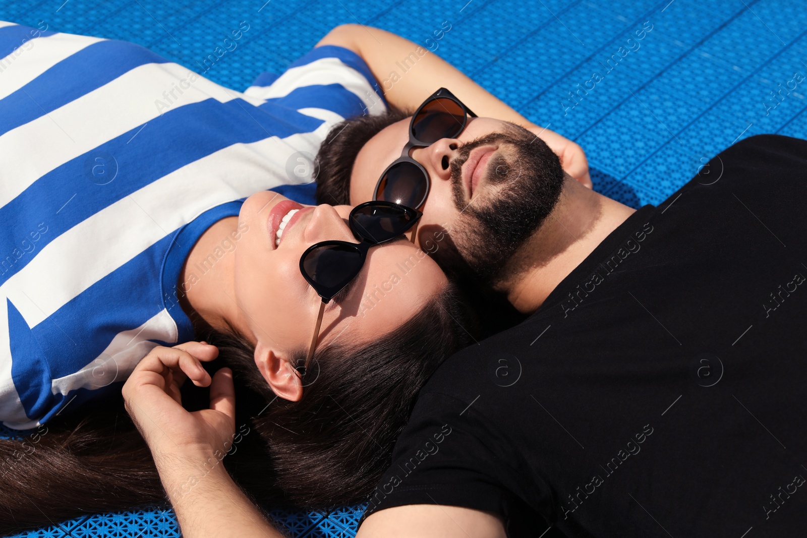 Photo of Beautiful smiling woman and handsome man in sunglasses on blue floor covering outdoors
