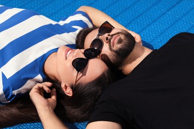 Beautiful smiling woman and handsome man in sunglasses on blue floor covering outdoors