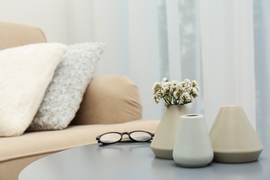 Photo of Beautiful ceramic vases and flowers on table in living room