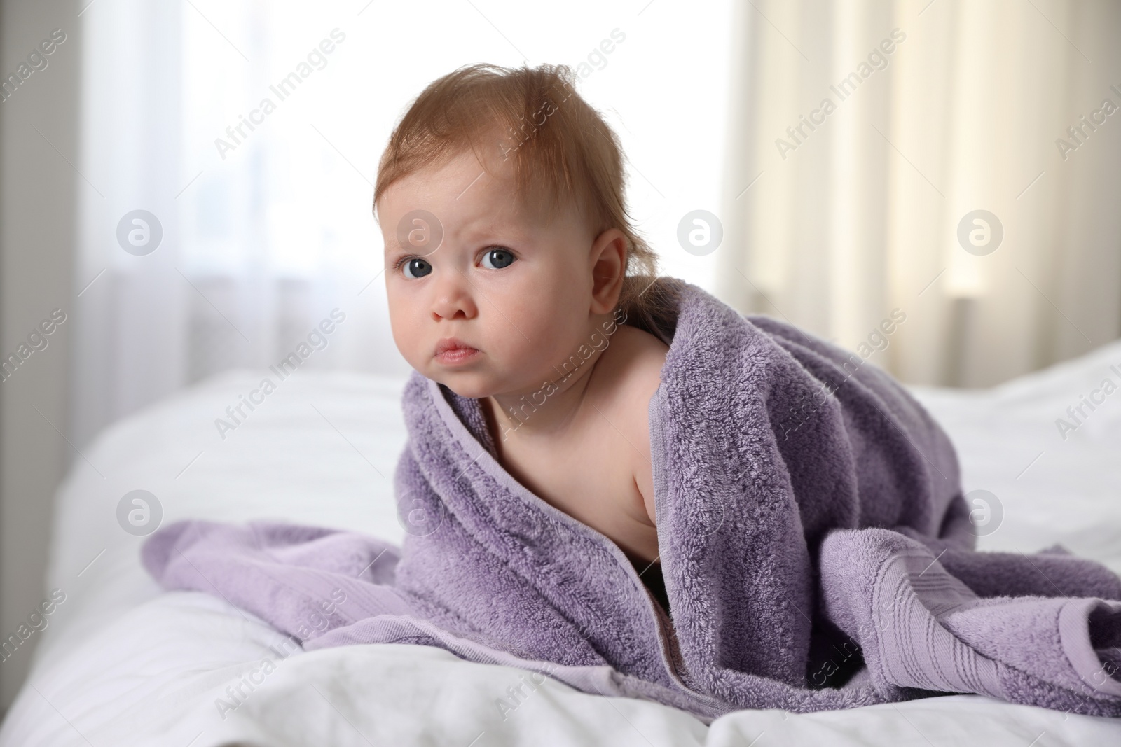 Photo of Cute little baby with soft purple towel on bed after bath