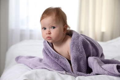 Cute little baby with soft purple towel on bed after bath