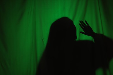 Silhouette of creepy ghost behind dark green cloth, space for text