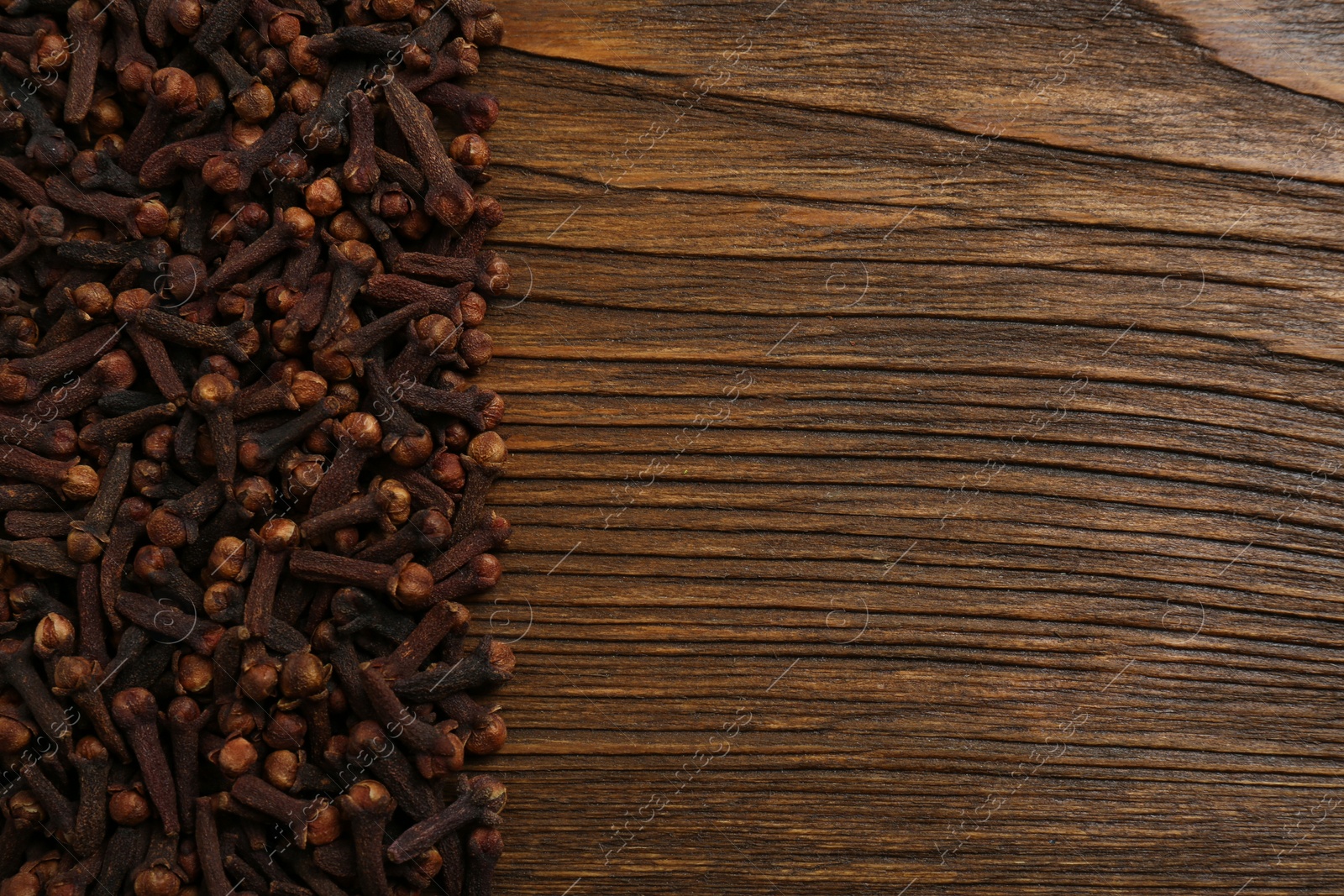 Photo of Aromatic dry cloves on wooden table, flat lay. Space for text