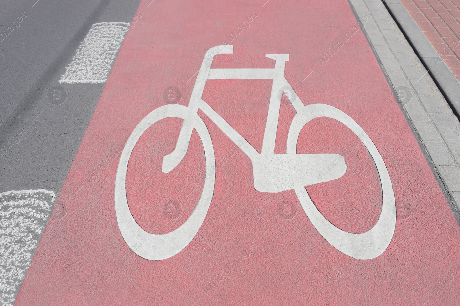 Photo of Red bike lane with painted white bicycle sign on sunny day