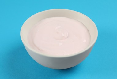 Photo of Bowl of tasty organic yogurt on light blue background