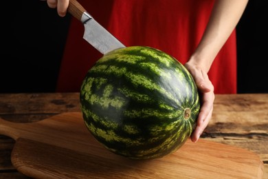 Woman cutting delicious watermelon at wooden table against black background, closeup