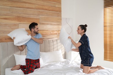 Photo of Happy couple in pajamas having pillow fight on bed at home