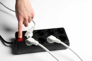 Photo of Woman pressing power button of extension cord on white background, closeup. Electrician's equipment