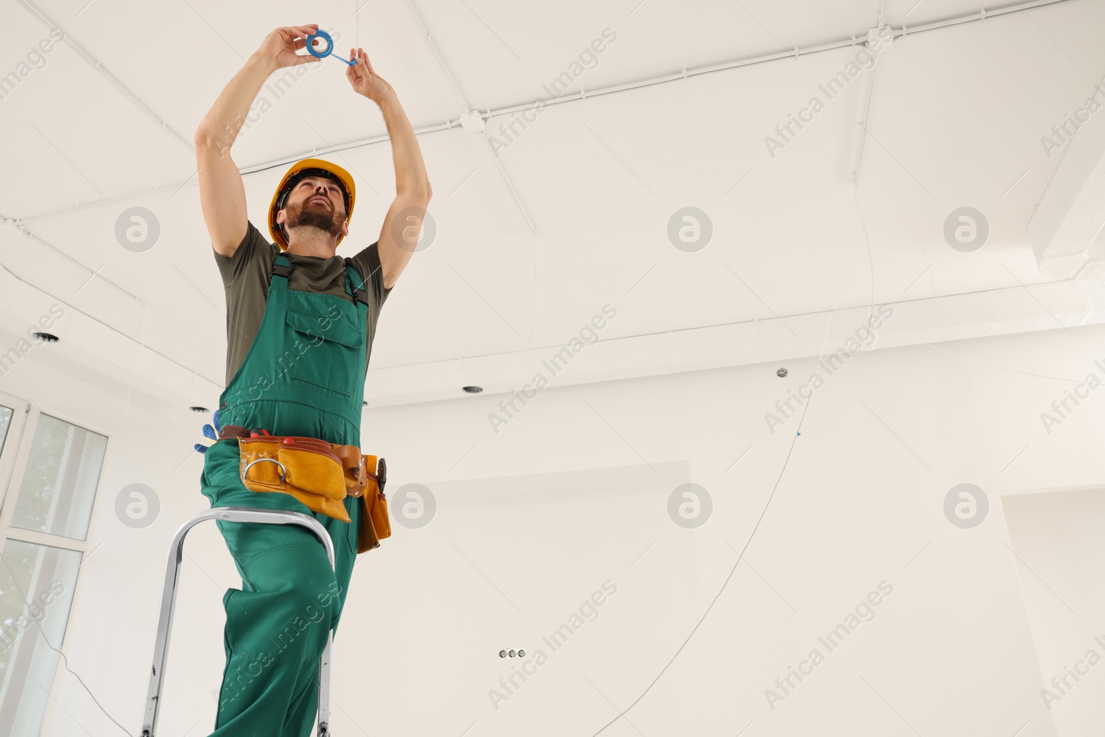 Photo of Electrician fixing wires with insulating tape indoors