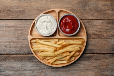Delicious fresh french fries and different sauces in bowls on wooden table, top view