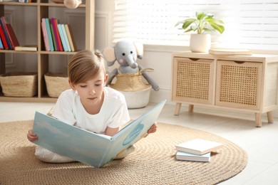 Photo of Little boy reading book on floor at home
