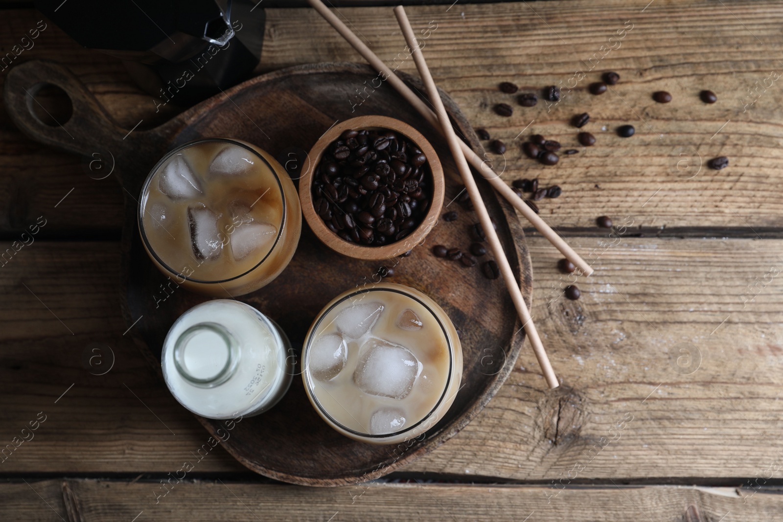 Photo of Refreshing iced coffee with milk in glasses, ingredients and straws on wooden table, flat lay. Space for text