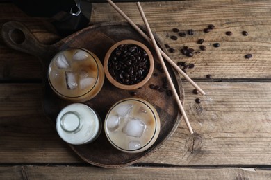 Photo of Refreshing iced coffee with milk in glasses, ingredients and straws on wooden table, flat lay. Space for text