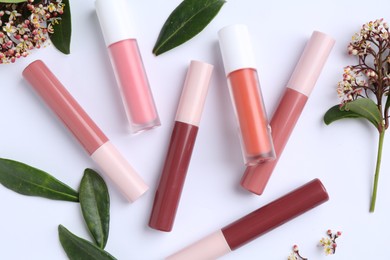 Photo of Different lip glosses, green leaves and flowers on white background, flat lay