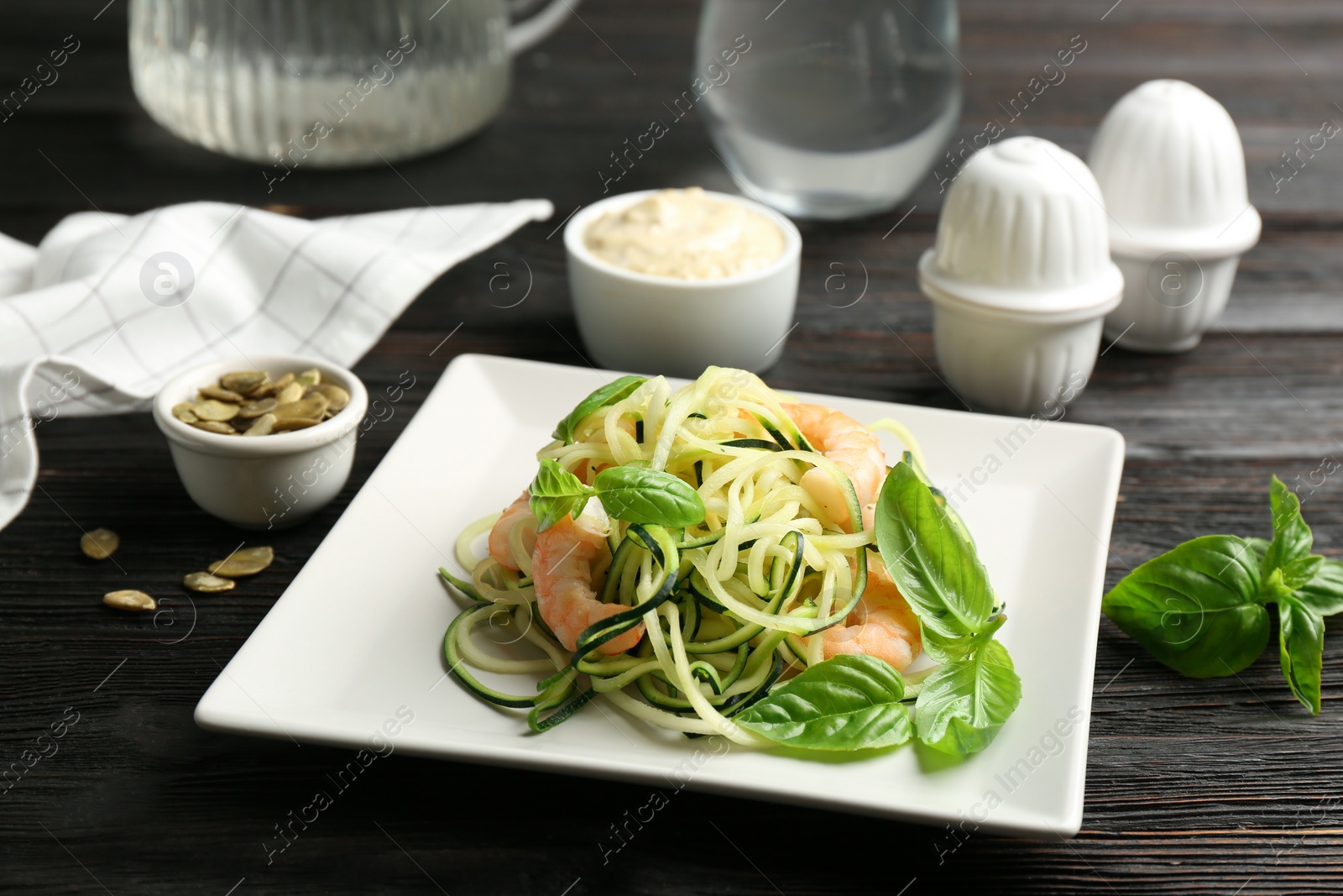 Photo of Delicious zucchini pasta with shrimps and basil served on black wooden table