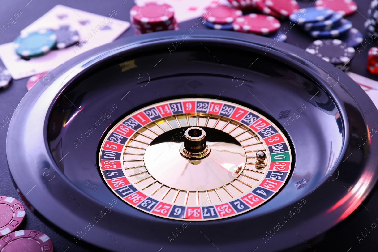 Photo of Roulette wheel, playing cards and chips on table, closeup. Casino game