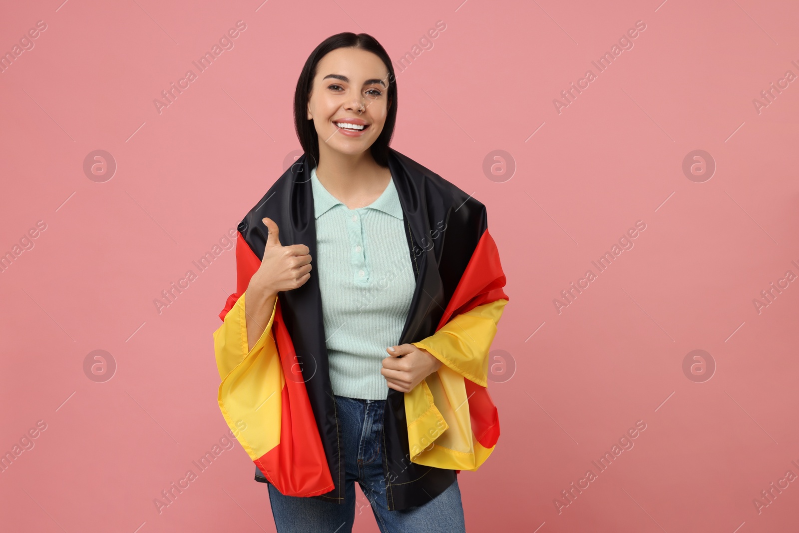 Photo of Happy young woman with flag of Germany showing thumbs up on pink background