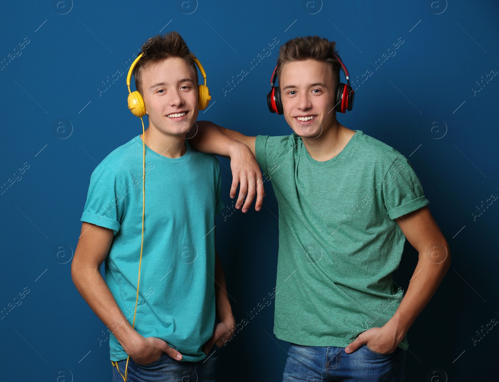 Photo of Teenage twin brothers with headphones on color background