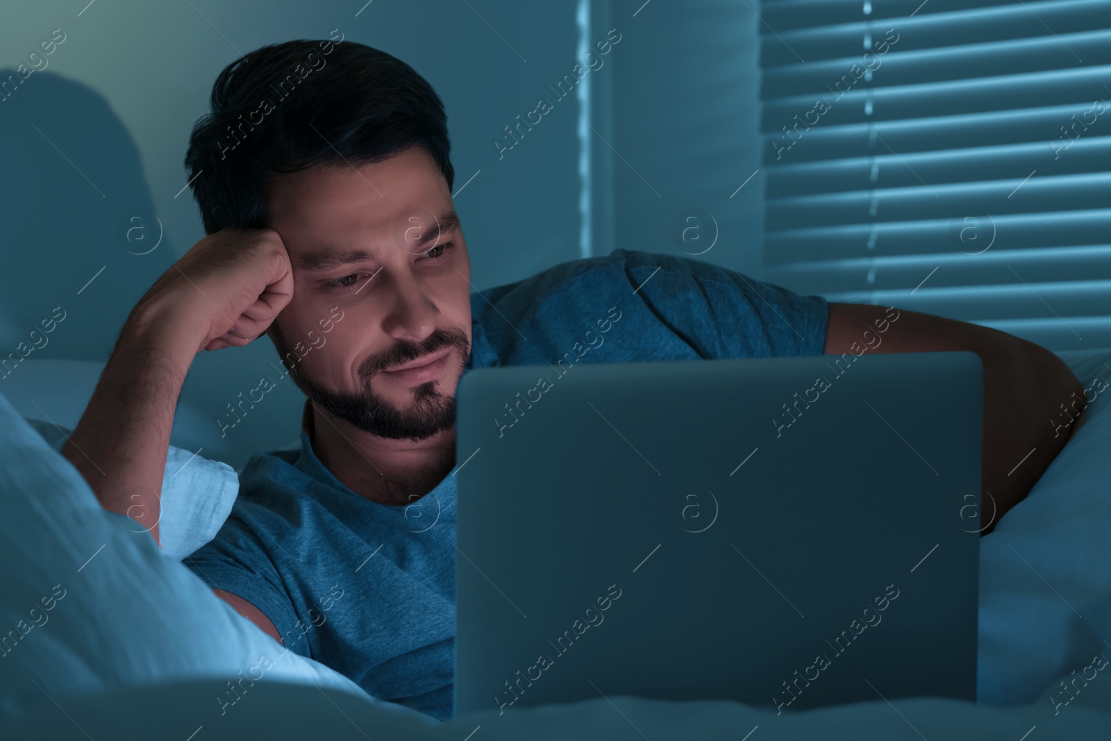 Photo of Man using laptop in bed at night. Internet addiction