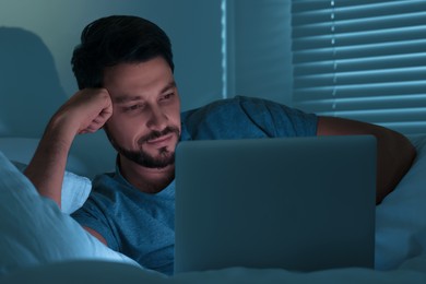 Photo of Man using laptop in bed at night. Internet addiction