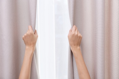 Woman opening window curtains at home, closeup