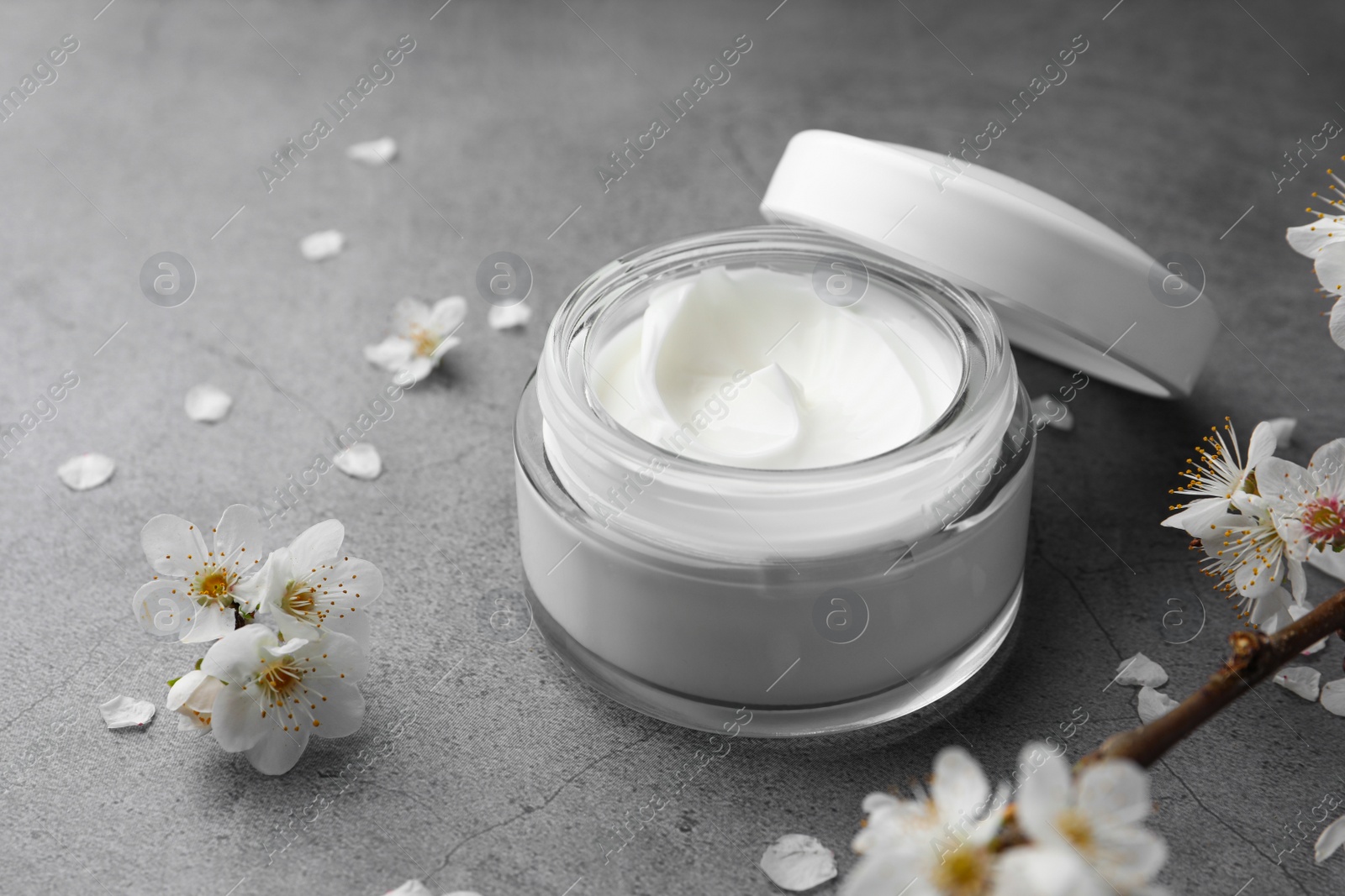 Photo of Jar of face cream and flowers on grey table. Space for text