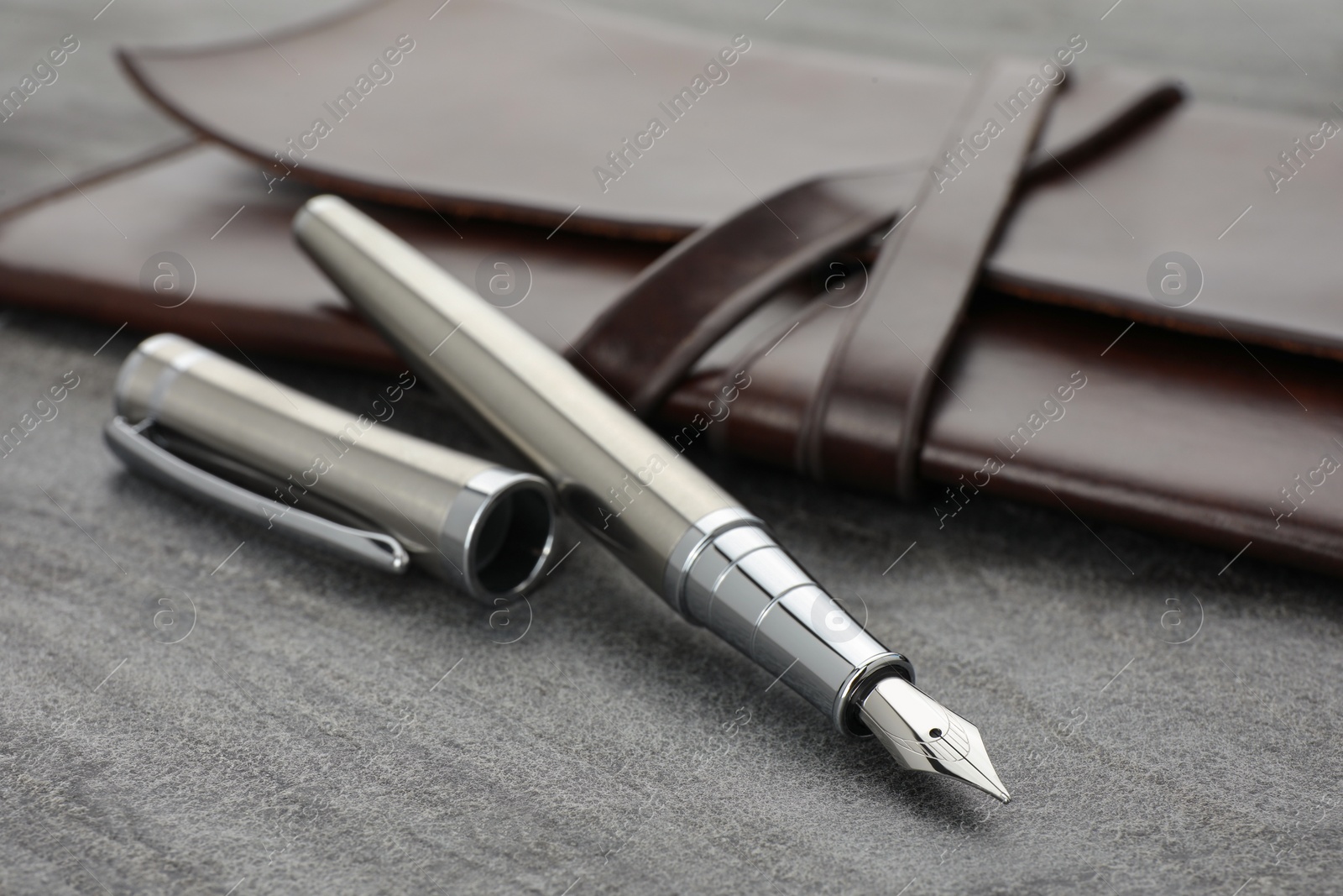 Photo of Stylish silver fountain pen and leather notebook on grey textured table, closeup