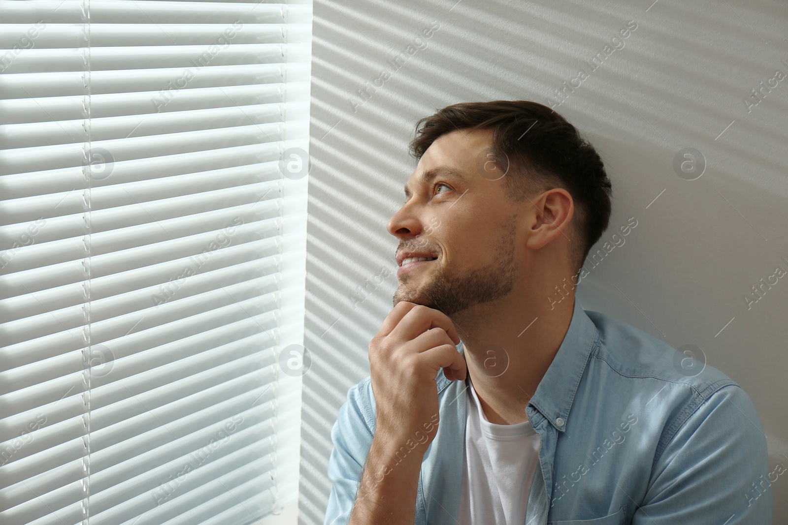 Photo of Handsome man near window with Venetian blinds. Space for text