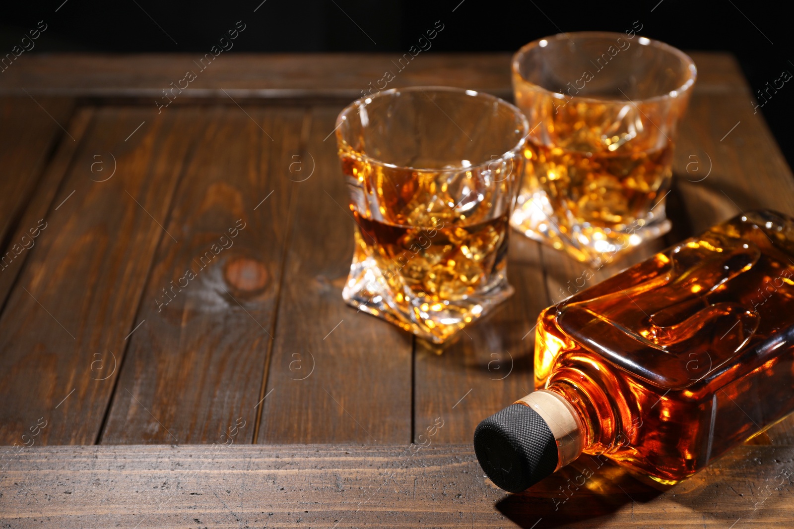 Photo of Whiskey with ice cubes in glasses and bottle on wooden crate, closeup. Space for text