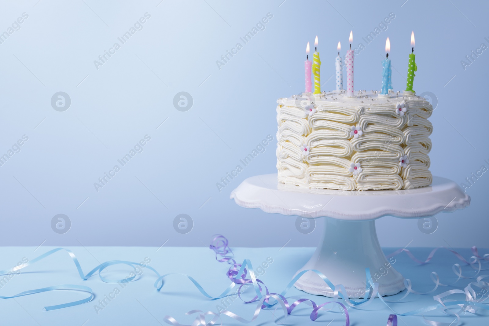 Photo of Delicious cake with burning candles and festive decor on light blue background. Space for text