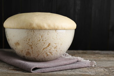 Photo of Bowl of fresh yeast dough on wooden table. Space for text