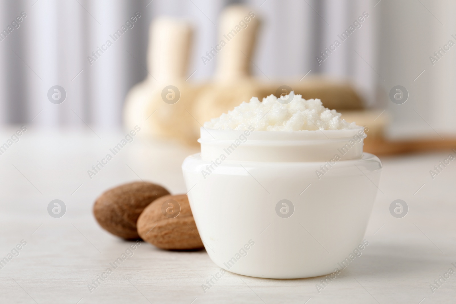 Photo of Jar of shea butter and nuts on table against blurred background. Space for text