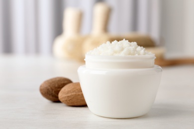 Jar of shea butter and nuts on table against blurred background. Space for text