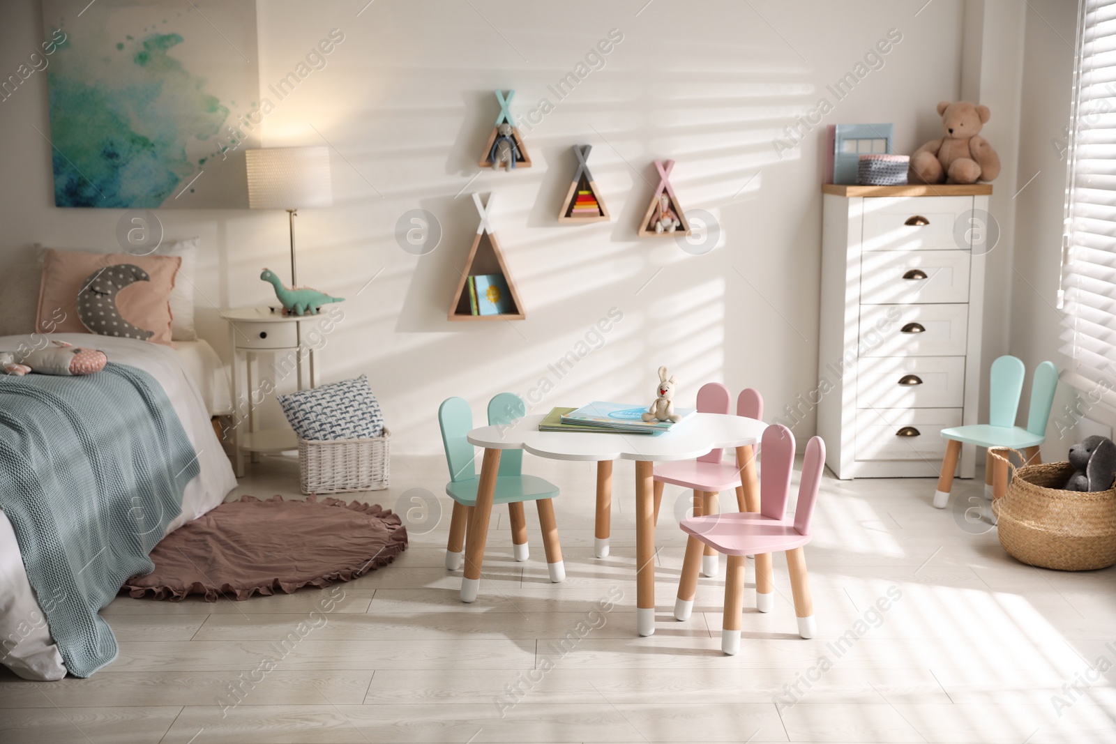 Photo of Small table and chairs with bunny ears in children's room interior