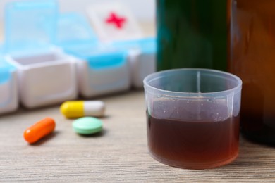 Photo of Measuring cup with syrup, pills on white table, closeup and space for text. Cold medicine