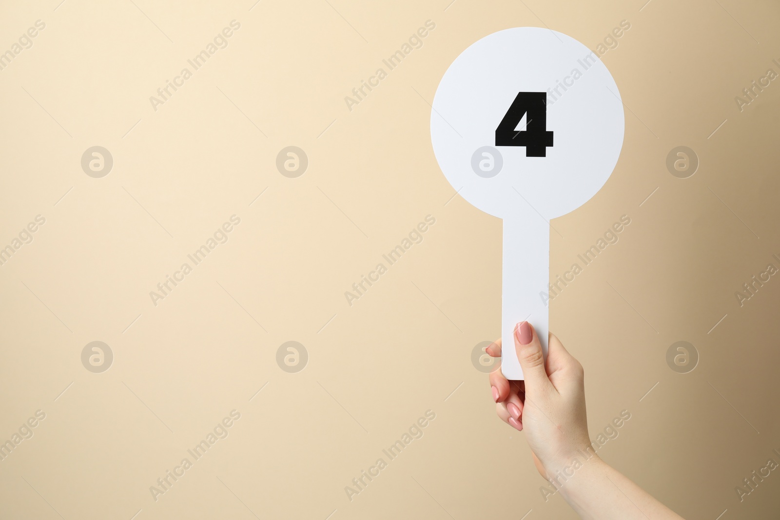 Photo of Woman holding auction paddle with number 4 on beige background, closeup. Space for text