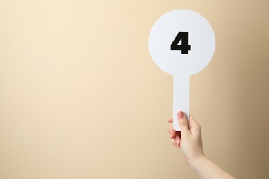 Woman holding auction paddle with number 4 on beige background, closeup. Space for text