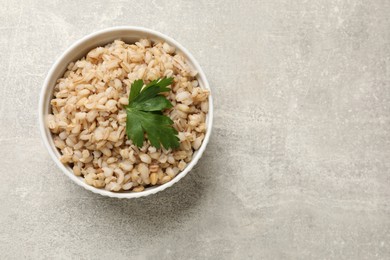 Photo of Tasty pearl barley porridge in bowl on light textured table, top view. Space for text