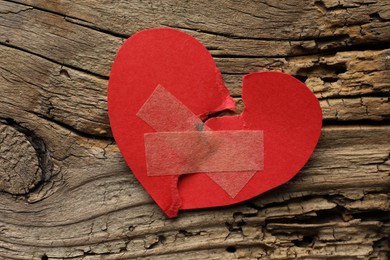 Photo of Broken heart. Torn red paper heart with medical adhesive bandages on wooden table, top view