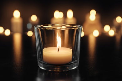 Burning candle on table in darkness. Funeral symbol