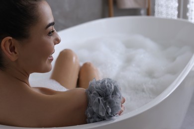 Photo of Woman taking bath with mesh pouf in bathroom, closeup