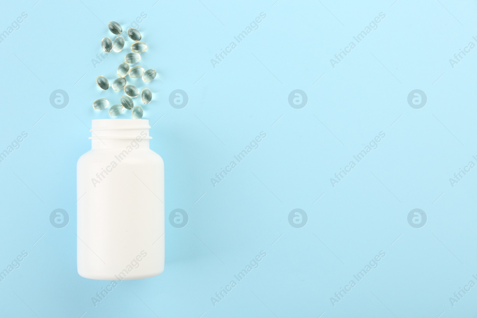 Photo of Bottle and vitamin capsules on light blue background, top view. Space for text